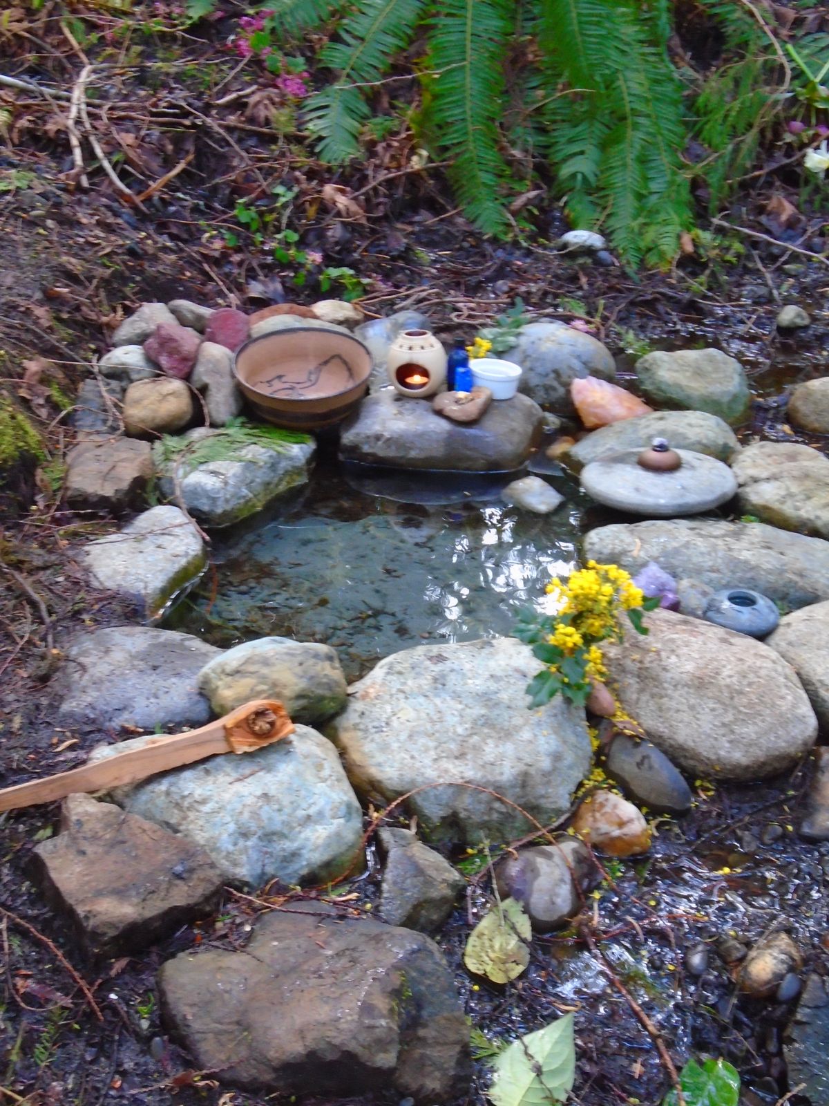 A ring of stones around a spring, with flowers and small offerings